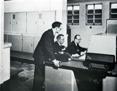 Computer pioneer Tom Kilburn (standing) and two colleagues at the Ferranti Mark I computer console